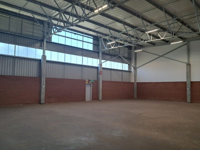 Spacious industrial warehouse unit featuring high ceilings with exposed steel trusses, concrete flooring, and ample natural light through high-level clerestory windows.