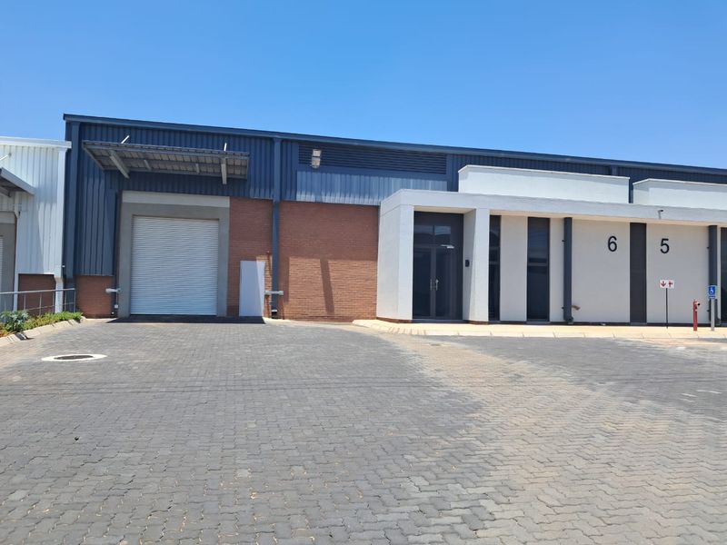 Front elevation of an industrial unit featuring a roller shutter door, paved driveway, and modern glass entrance.