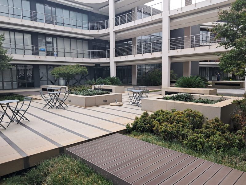 A modern multi-level office courtyard featuring paved walkways, raised planter boxes, and integrated landscaping between building wings.