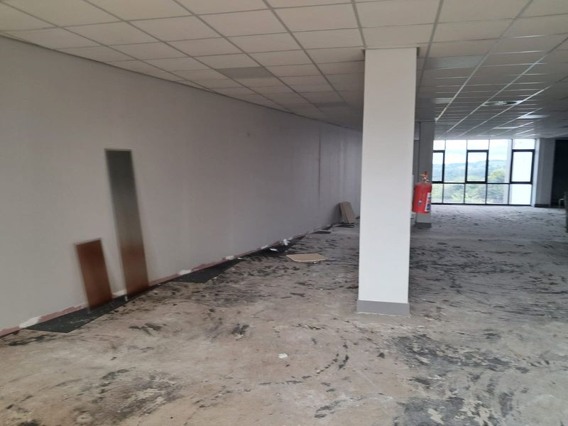 An empty, open-plan office space featuring a suspended ceiling, structural column, and large windows with natural light, currently requiring flooring installation.