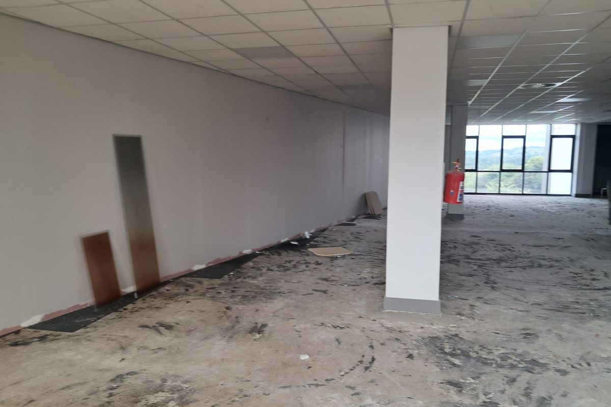 An empty, open-plan office space featuring a suspended ceiling, structural column, and large windows with natural light, currently requiring flooring installation.