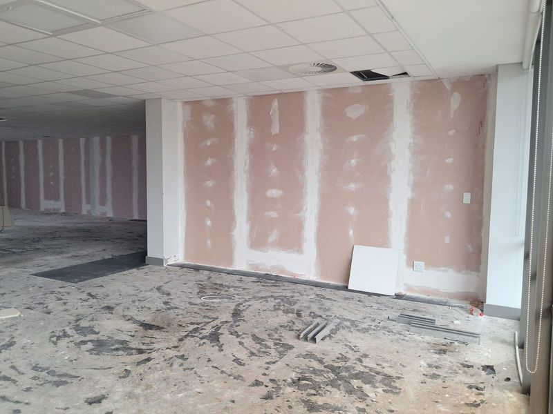 An unfinished office space featuring exposed drywall, a suspended ceiling with missing tiles, and an exposed subfloor, ready for renovation and fit-out.