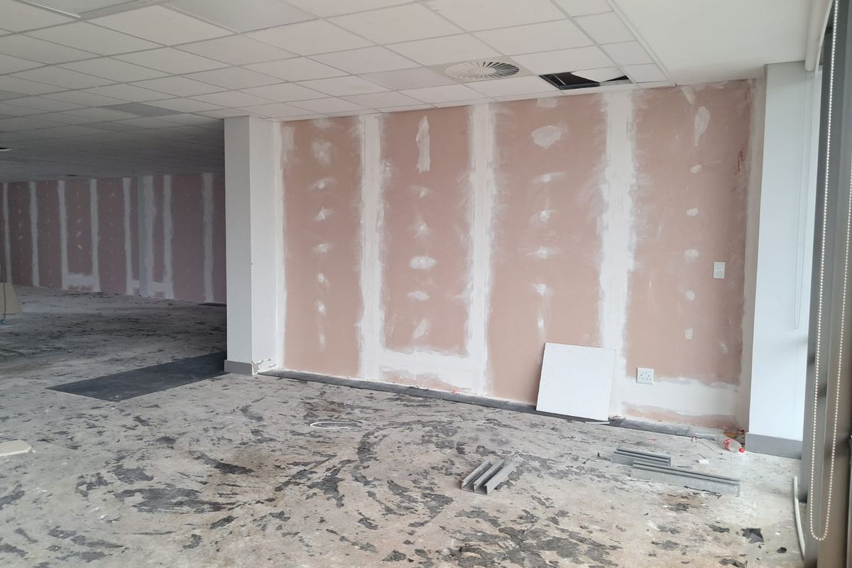 An unfinished office space featuring exposed drywall, a suspended ceiling with missing tiles, and an exposed subfloor, ready for renovation and fit-out.