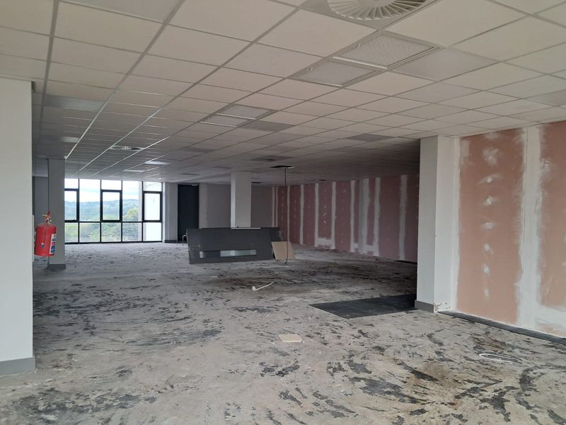 Open-plan office space in shell condition, featuring large windows, suspended ceiling, and unfinished wall surfaces ready for custom fit-out.