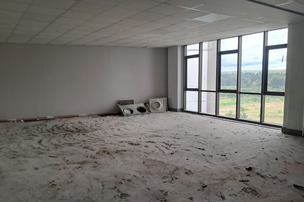 An empty, unfinished office space featuring large floor-to-ceiling windows with natural light and a suspended ceiling, requiring flooring and finishing work.