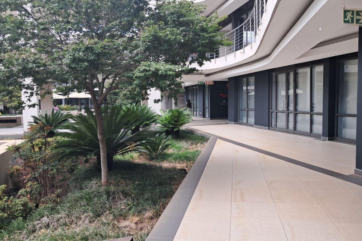 A modern office building exterior featuring a paved walkway, glass facade, and well-maintained landscaped garden area.