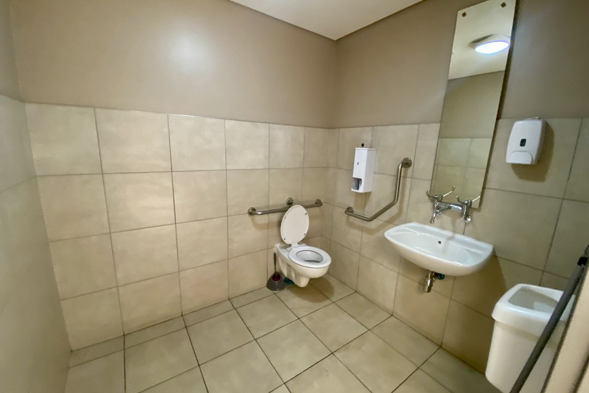 A functional, accessible bathroom featuring tiled walls and flooring, a wall-mounted basin, and grab rails for accessibility.