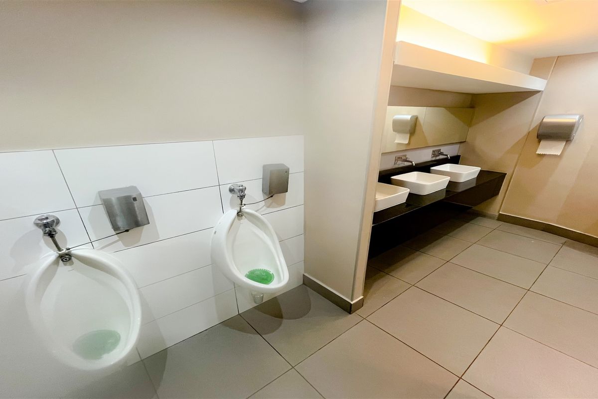 A clean, modern commercial restroom featuring wall-mounted urinals, a sleek vanity with multiple basins, and large-format floor tiling.