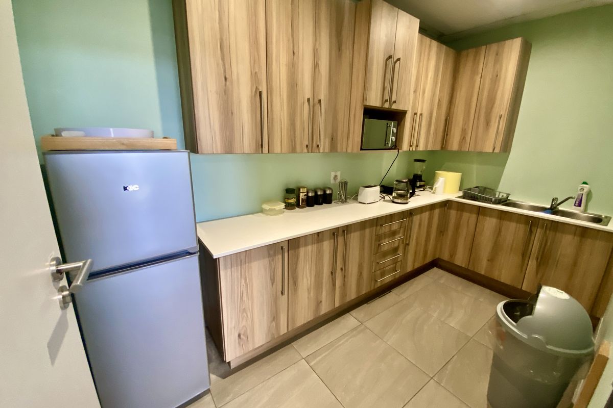 A functional kitchen area featuring wood-grain cabinetry, light-colored countertops, a stainless steel sink, and tiled flooring.