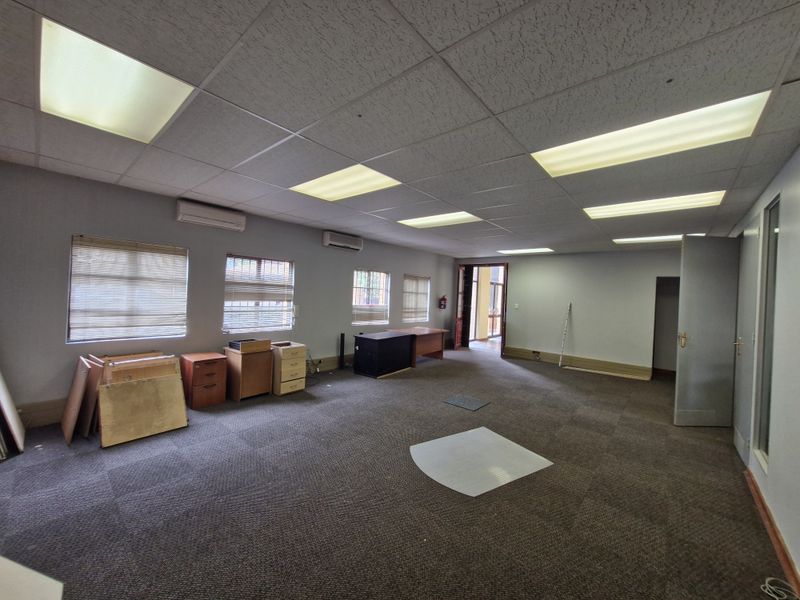 Spacious commercial office area featuring suspended ceilings, recessed lighting, wall-mounted air conditioning units, and carpeted flooring.