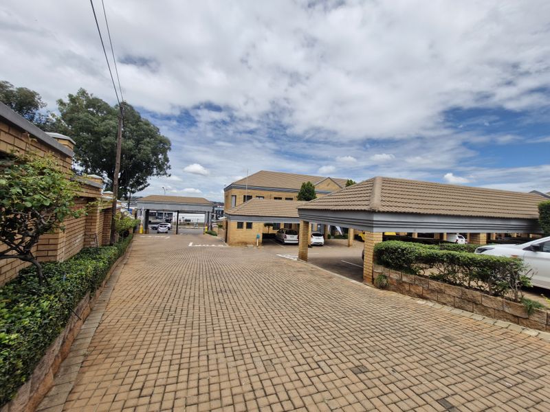 Commercial property entrance featuring extensive brick paving, covered parking structures, and well-maintained brick boundary walls.