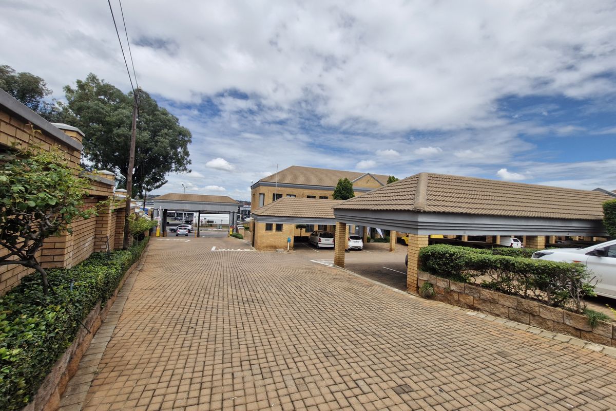 Commercial property entrance featuring extensive brick paving, covered parking structures, and well-maintained brick boundary walls.