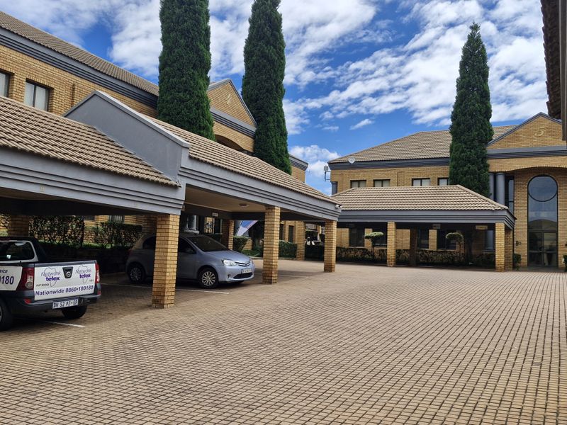 Commercial office complex exterior featuring brick paved parking area with covered bays and well-maintained brick building facades.