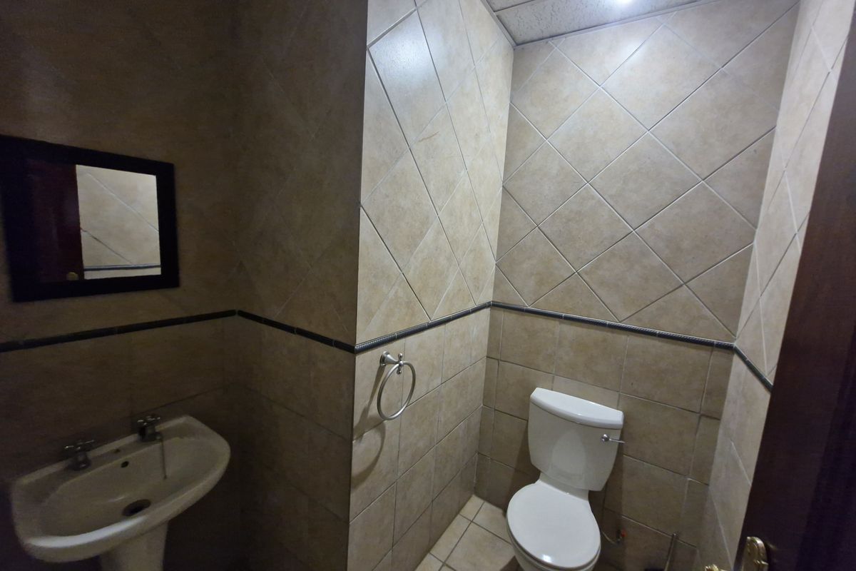 A functional bathroom featuring tiled walls and flooring, equipped with a pedestal basin and a standard toilet.