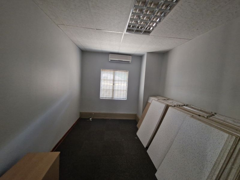 A vacant office space featuring a suspended ceiling with recessed lighting, a wall-mounted air conditioning unit, and carpeted flooring.