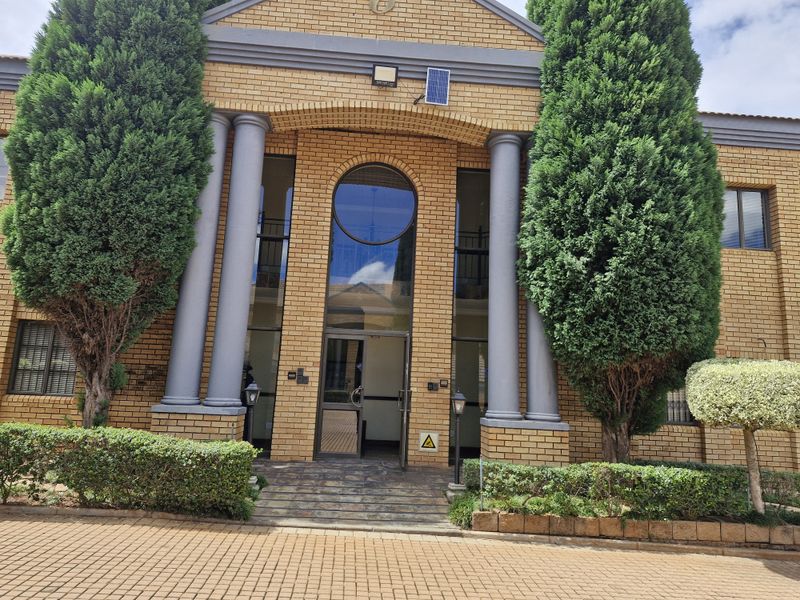 A professional commercial building facade featuring classic brickwork, prominent columns, a circular window, and a paved entrance area with manicured landscaping.