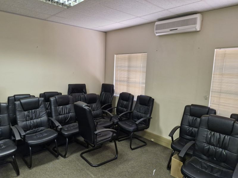A functional office space featuring carpeted flooring, suspended ceiling tiles, wall-mounted air conditioning, and venetian blinds on the windows.