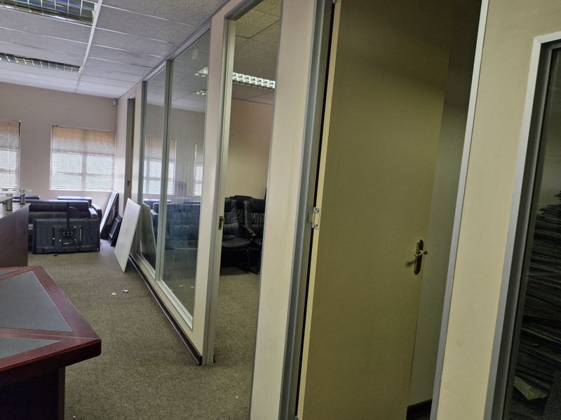 Commercial office space featuring glass partition walls, suspended ceilings with recessed lighting, and carpeted flooring, providing a functional layout for professional use.