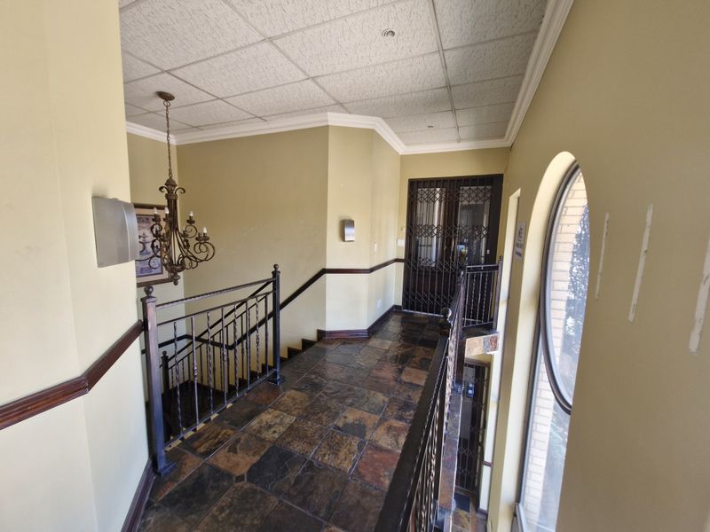 A spacious upper-level hallway featuring slate tile flooring, wrought iron balustrades, and an arched window, providing access to secure entry points.