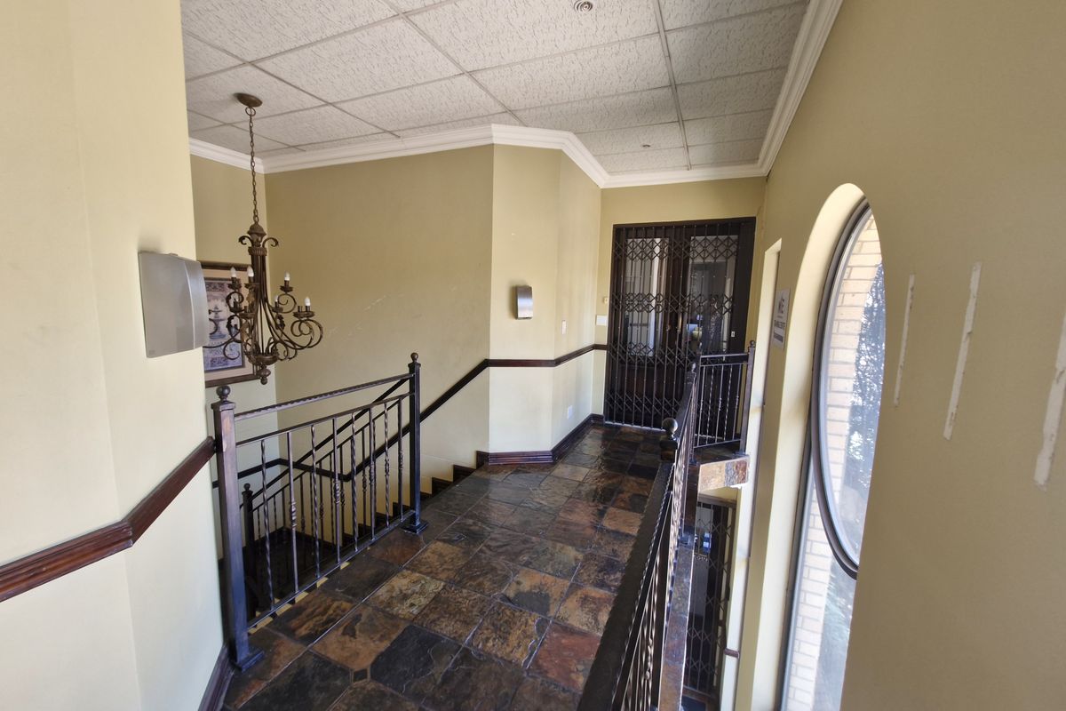 A spacious upper-level hallway featuring slate tile flooring, wrought iron balustrades, and an arched window, providing access to secure entry points.