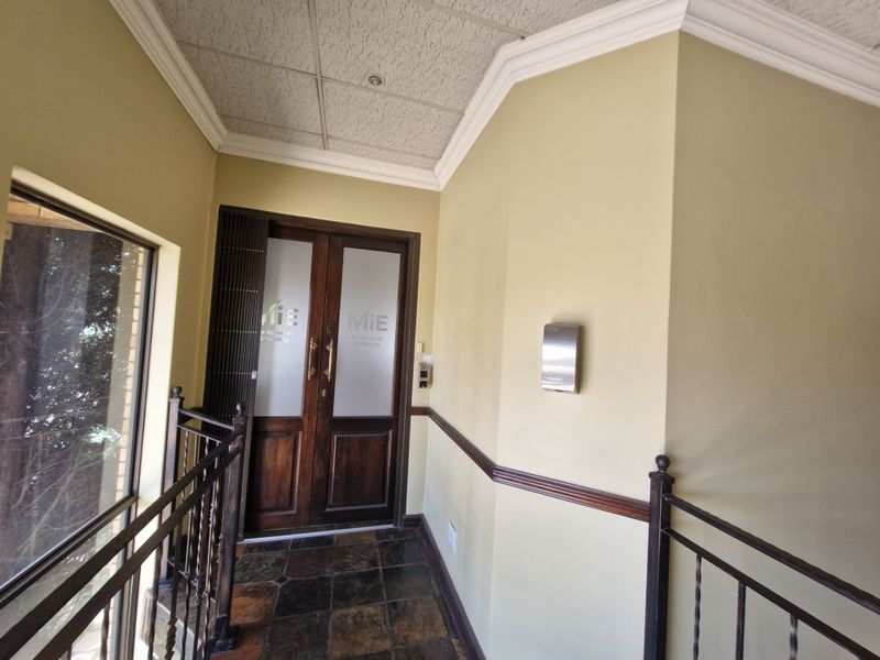 A commercial entrance foyer featuring double wooden doors with frosted glass, slate tile flooring, and a decorative wrought iron balustrade.
