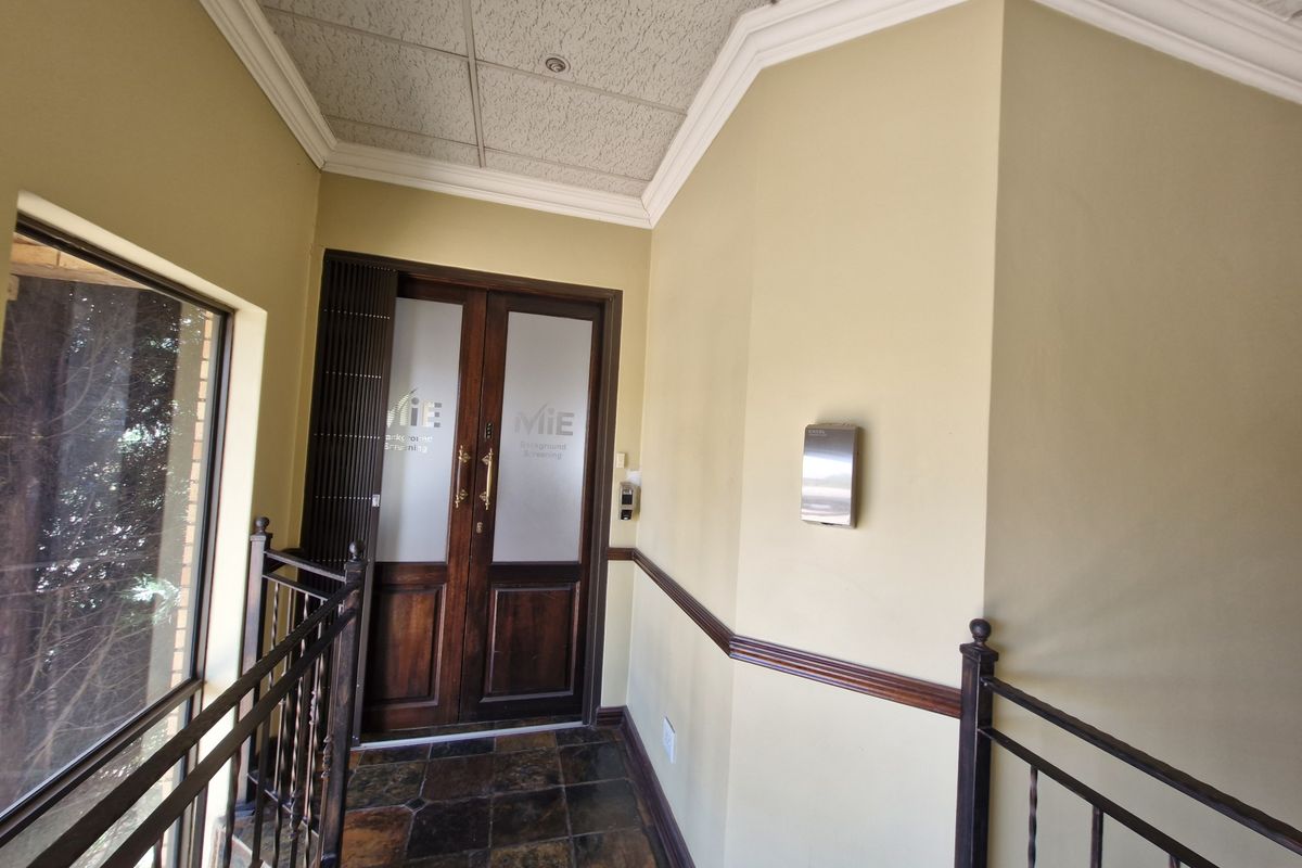 A commercial entrance foyer featuring double wooden doors with frosted glass, slate tile flooring, and a decorative wrought iron balustrade.
