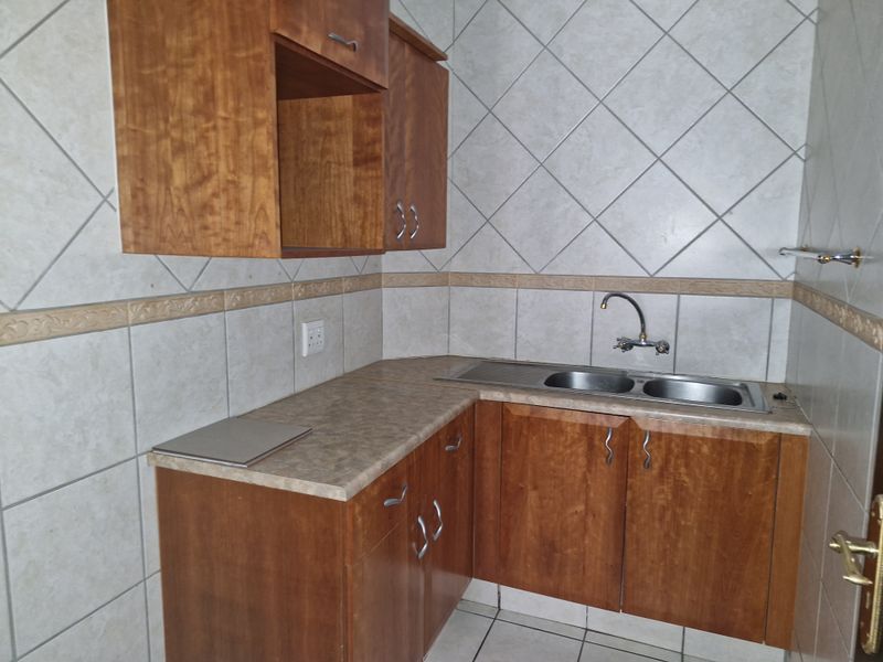A functional kitchen area featuring wooden cabinetry, laminate countertops, a double stainless steel sink, and tiled wall finishes.