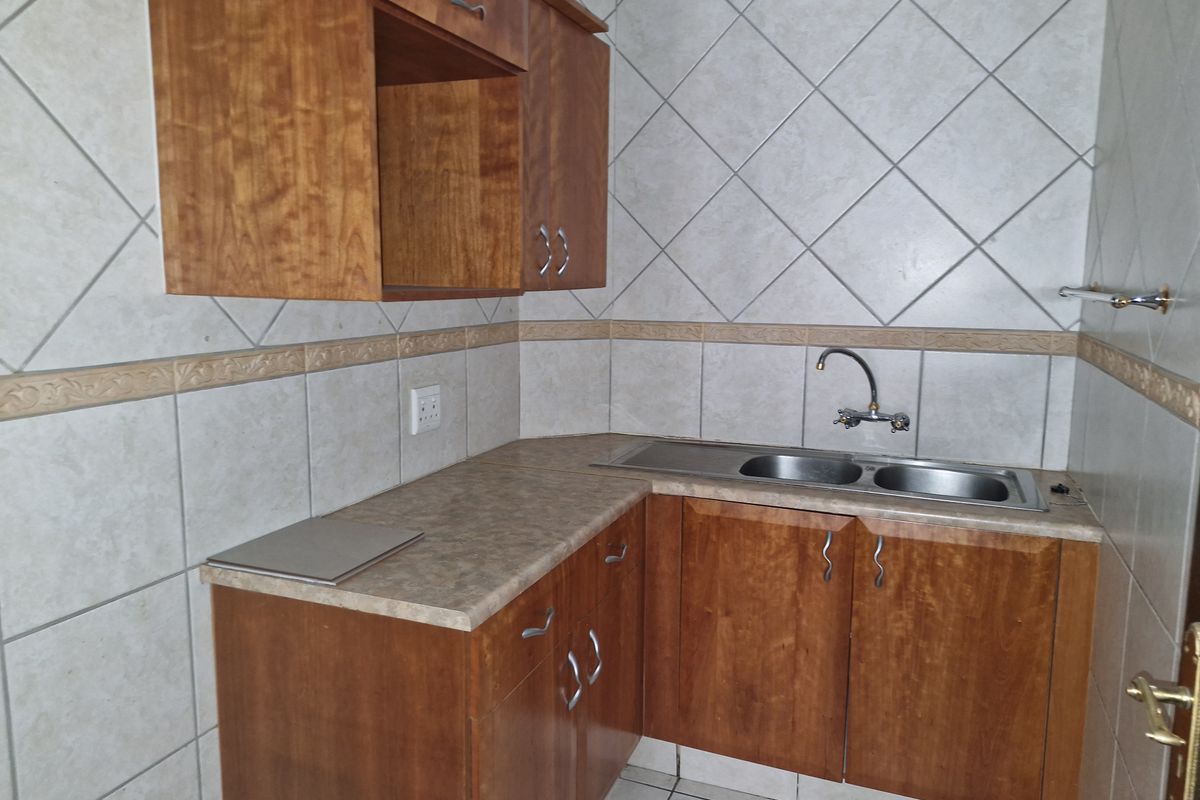 A functional kitchen area featuring wooden cabinetry, laminate countertops, a double stainless steel sink, and tiled wall finishes.