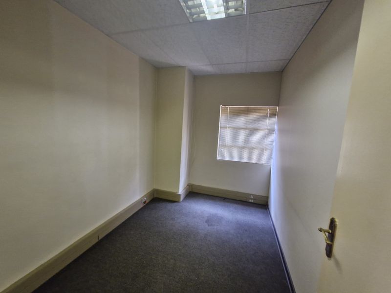 A vacant office space featuring a suspended ceiling, recessed lighting, window blinds, and carpeted flooring, suitable for a professional workspace.
