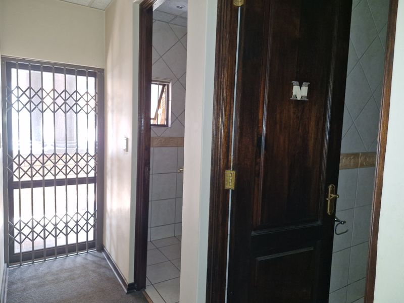 A functional commercial hallway featuring tiled flooring, a security gate, and access to adjacent rooms with tiled wall finishes.