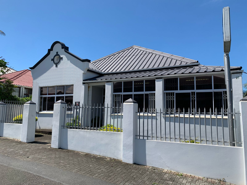 Front elevation of a commercial property featuring a gabled roof, secure metal fencing, and paved driveway access.