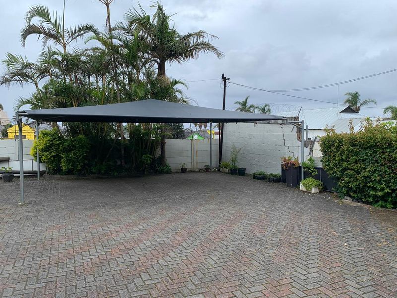 Paved outdoor parking area featuring a shade sail structure and perimeter wall with security fencing.