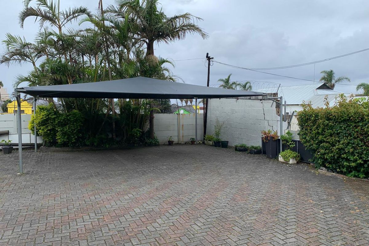 Paved outdoor parking area featuring a shade sail structure and perimeter wall with security fencing.