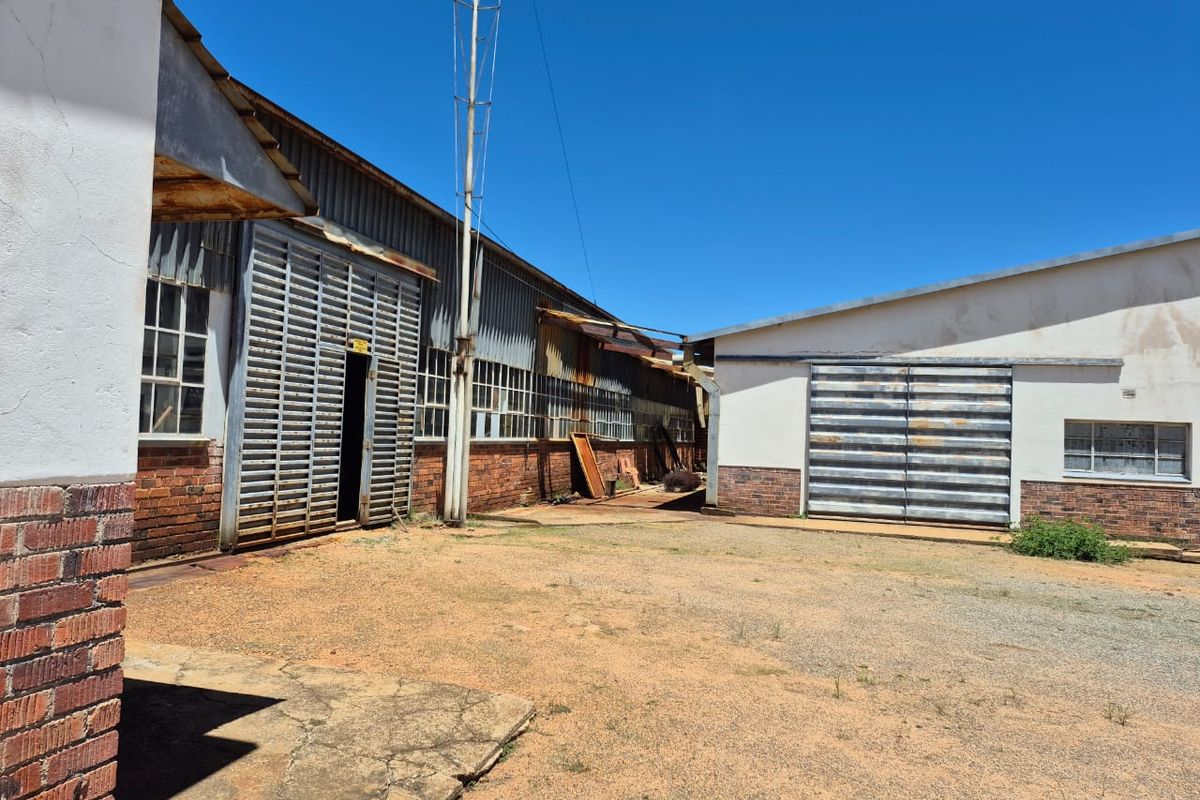 Exterior view of an industrial facility featuring brick and corrugated metal construction with large sliding access doors and a gravel yard area.