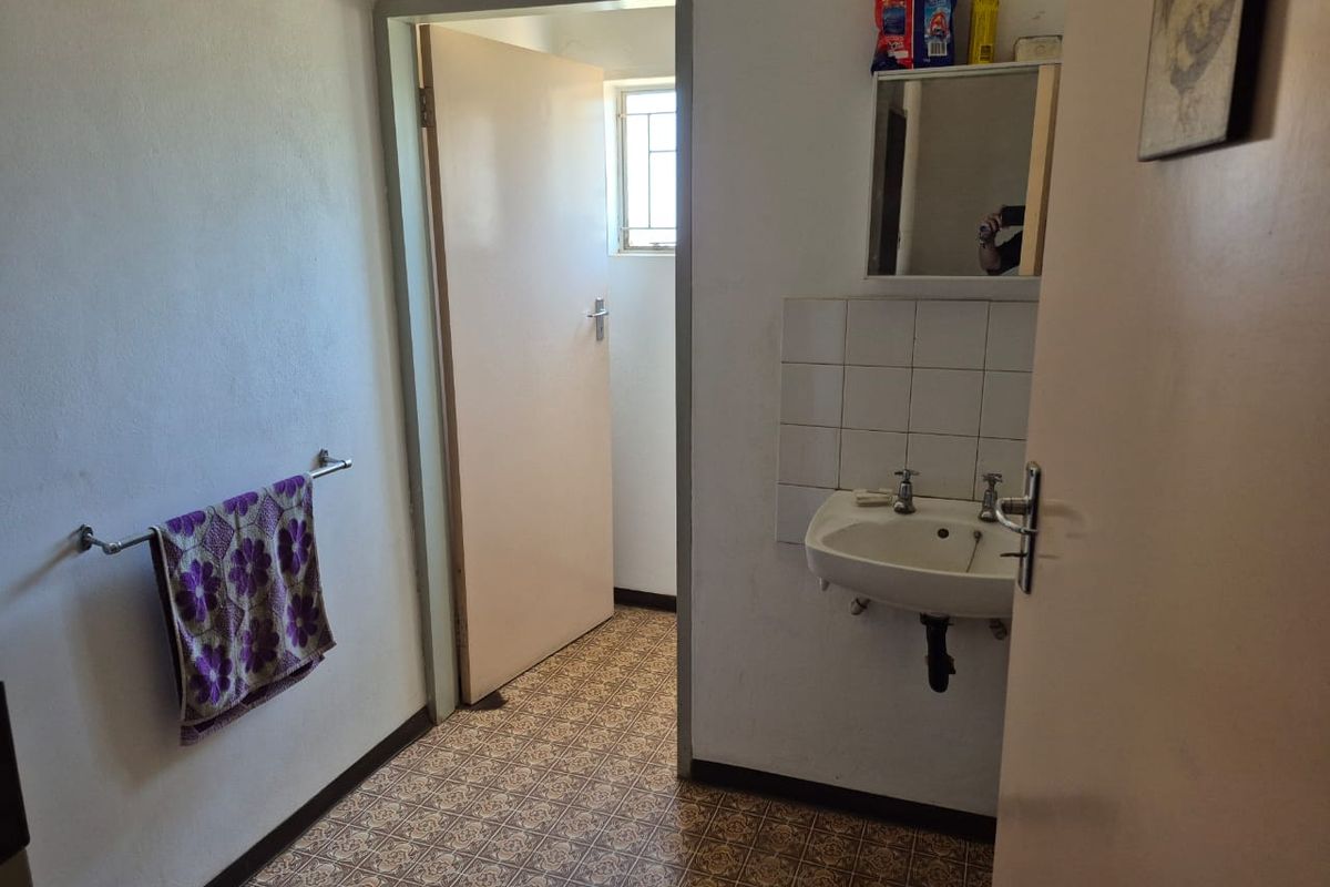A functional bathroom featuring a wall-mounted basin, tiled splashback, and patterned vinyl flooring, providing basic utility within the industrial property.