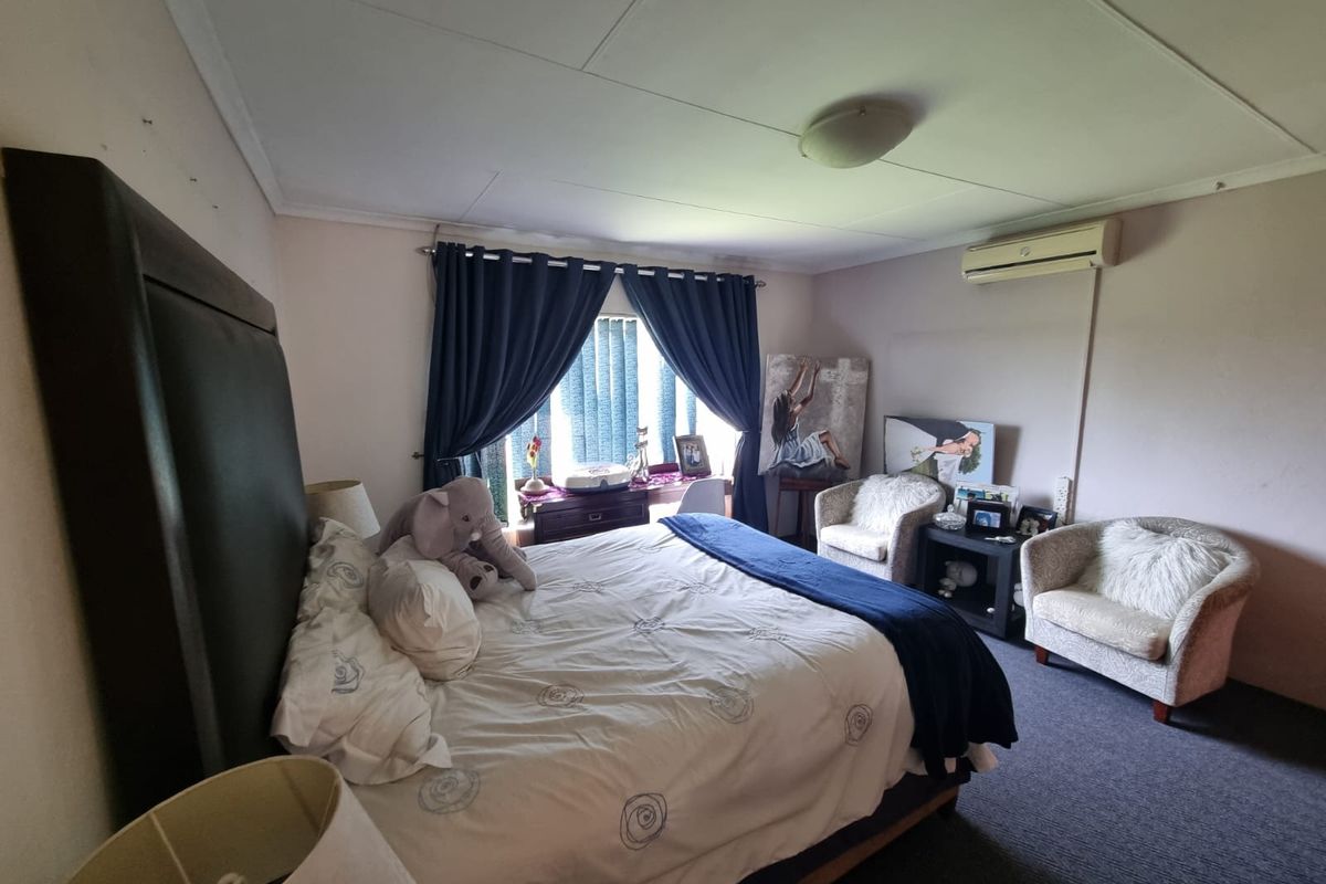 A spacious bedroom featuring carpeted flooring, a wall-mounted air conditioning unit, and large windows with curtains.