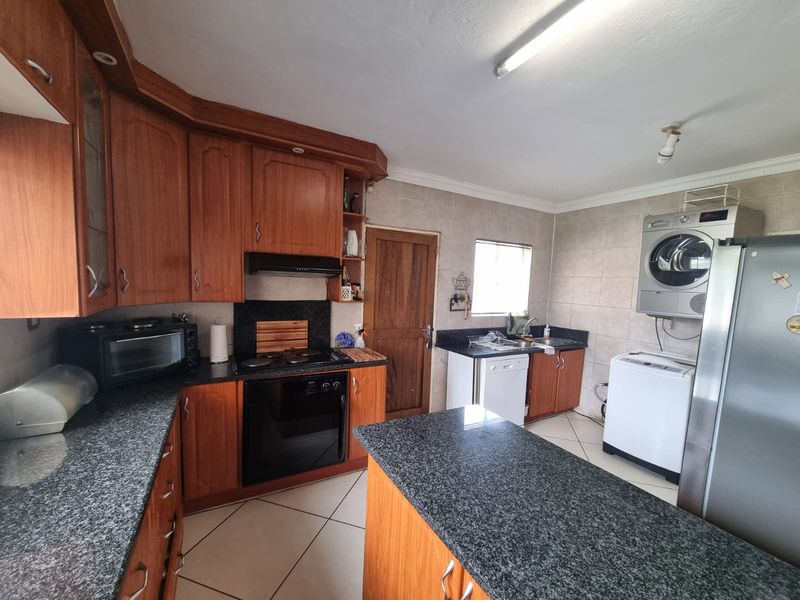 A functional kitchen featuring wooden cabinetry, granite countertops, built-in oven, extractor fan, and tiled flooring with an integrated laundry area.