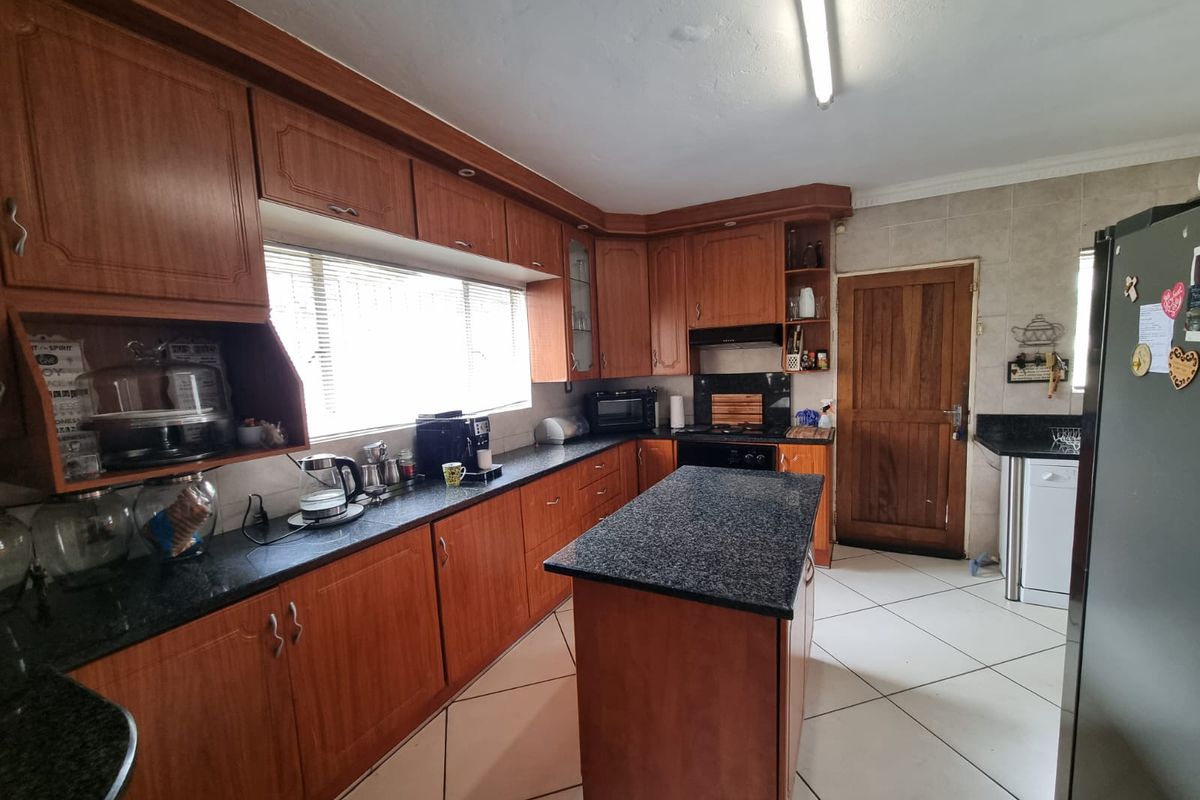A functional kitchen featuring wooden cabinetry, granite countertops, a central island, and tiled flooring, providing ample workspace and storage.