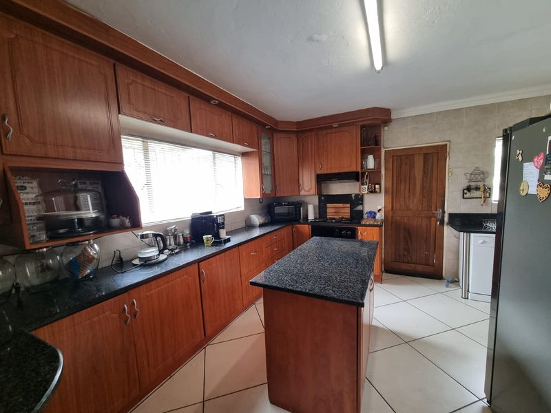 A functional kitchen featuring wooden cabinetry, granite countertops, a central island, and tiled flooring, providing ample workspace and storage.