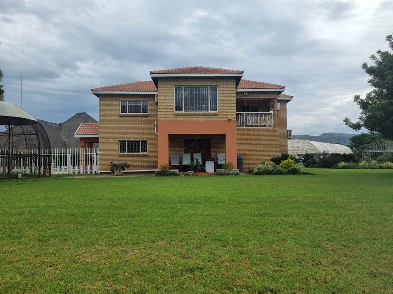 Rear view of a two-story face brick farmhouse featuring a tiled roof, a covered patio area, and a spacious surrounding lawn.