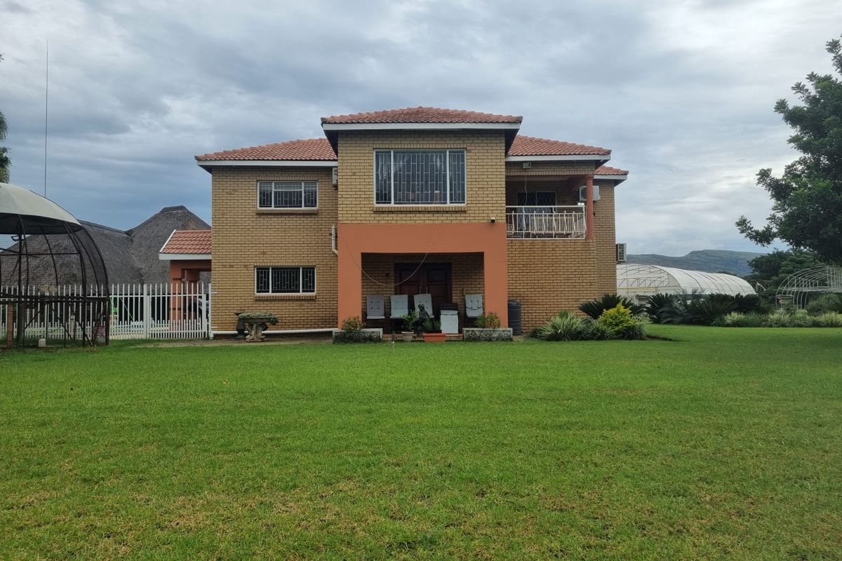 Rear view of a two-story face brick farmhouse featuring a tiled roof, a covered patio area, and a spacious surrounding lawn.