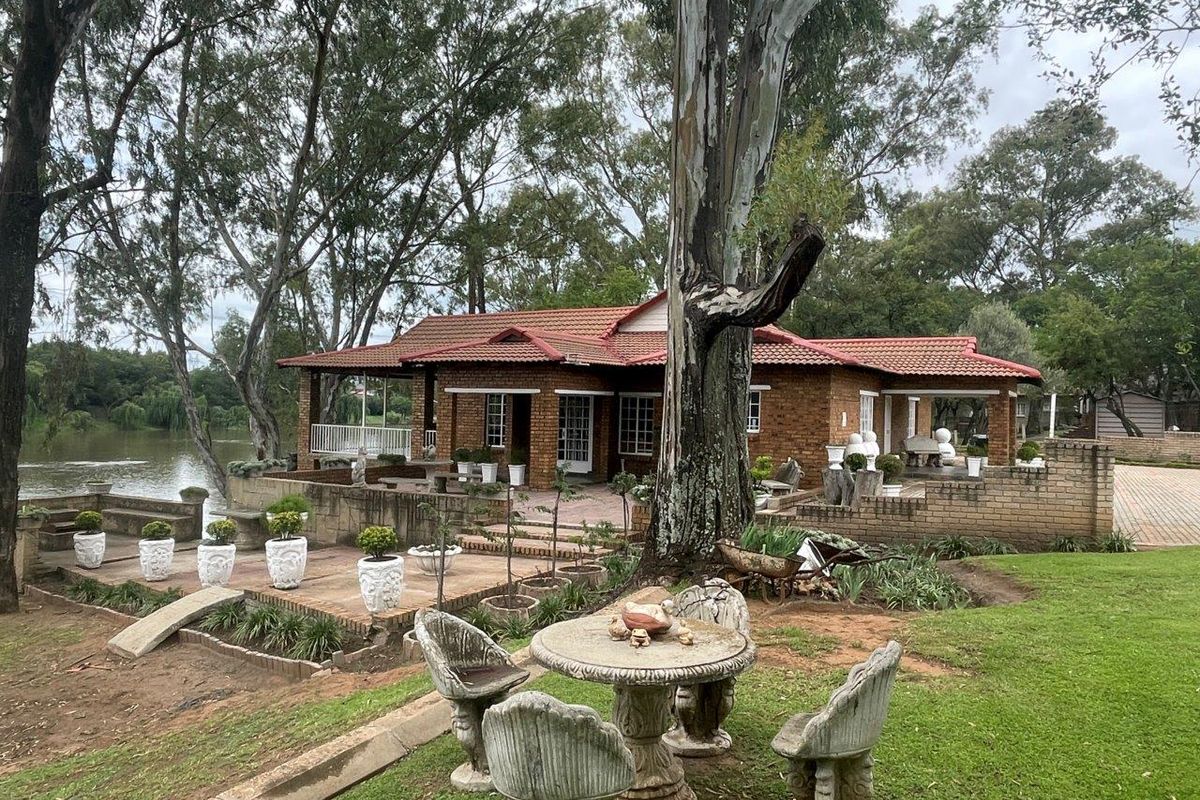 A charming face-brick small holding residence featuring a covered patio, expansive paved terrace, and direct waterfront access set within a mature garden.