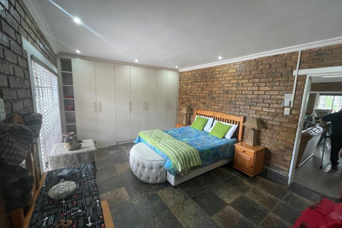 Spacious bedroom featuring an exposed brick feature wall, slate tile flooring, and extensive built-in cupboard storage with integrated shelving.
