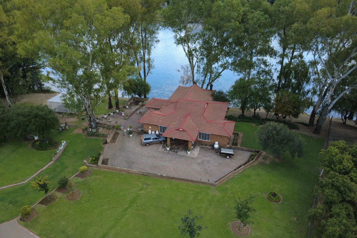 Aerial view of a residential small holding featuring a tiled roof dwelling, expansive lawn, paved driveway, and direct access to a waterfront area.