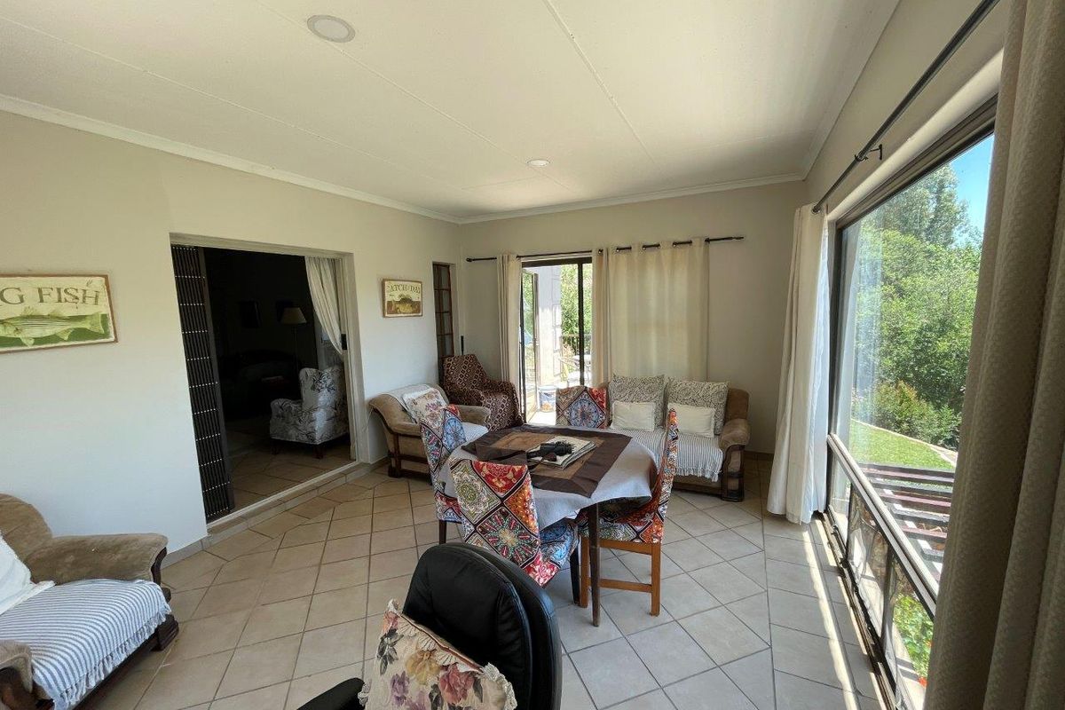A sunlit living area featuring tiled flooring, large windows with garden views, and sliding door access to the outdoor space.