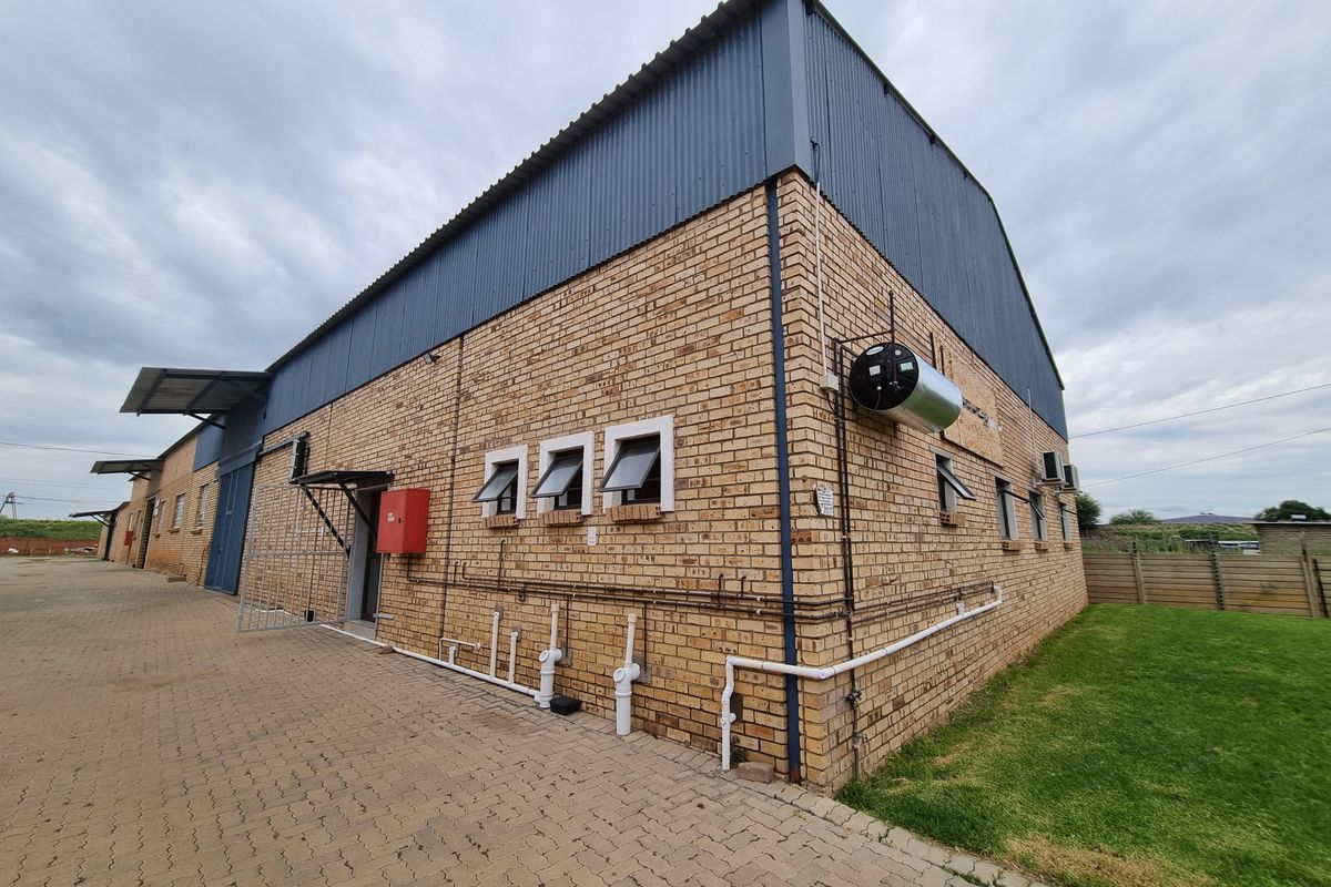 Rear view of a commercial warehouse building featuring face brick walls, corrugated metal roofing, external geyser, and paved driveway access.