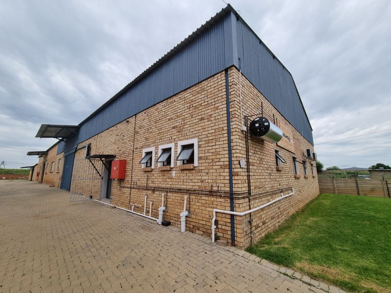 Rear view of a commercial warehouse building featuring face brick walls, corrugated metal roofing, external geyser, and paved driveway access.