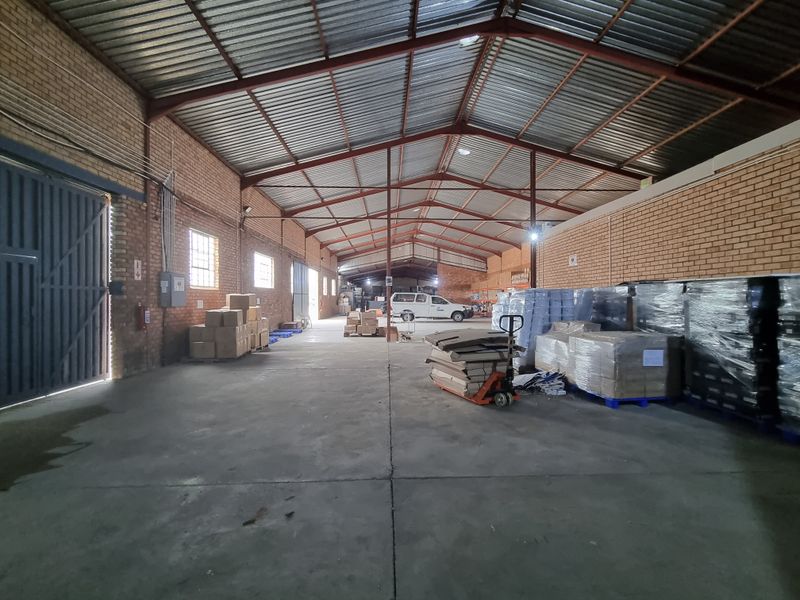 Spacious industrial warehouse featuring exposed brick walls, high-clearance corrugated metal roofing with steel trusses, and durable concrete flooring with large sliding access doors.