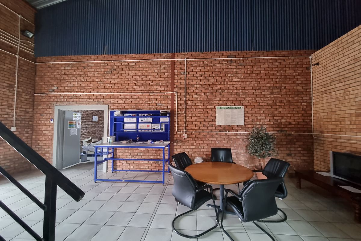 A functional commercial utility space featuring exposed brick walls, high corrugated metal ceilings, and tiled flooring, suitable for office or workshop use.