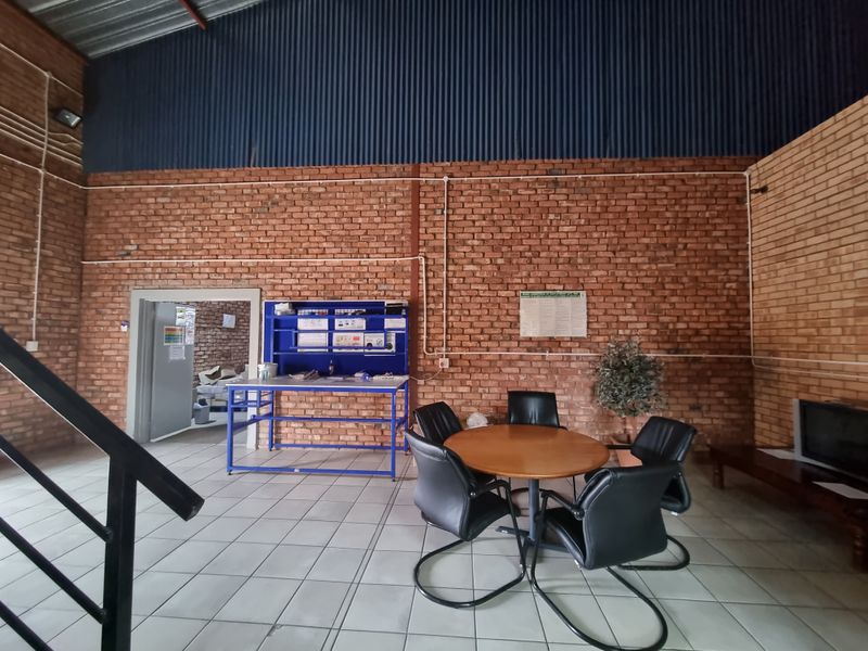 A functional commercial utility space featuring exposed brick walls, high corrugated metal ceilings, and tiled flooring, suitable for office or workshop use.